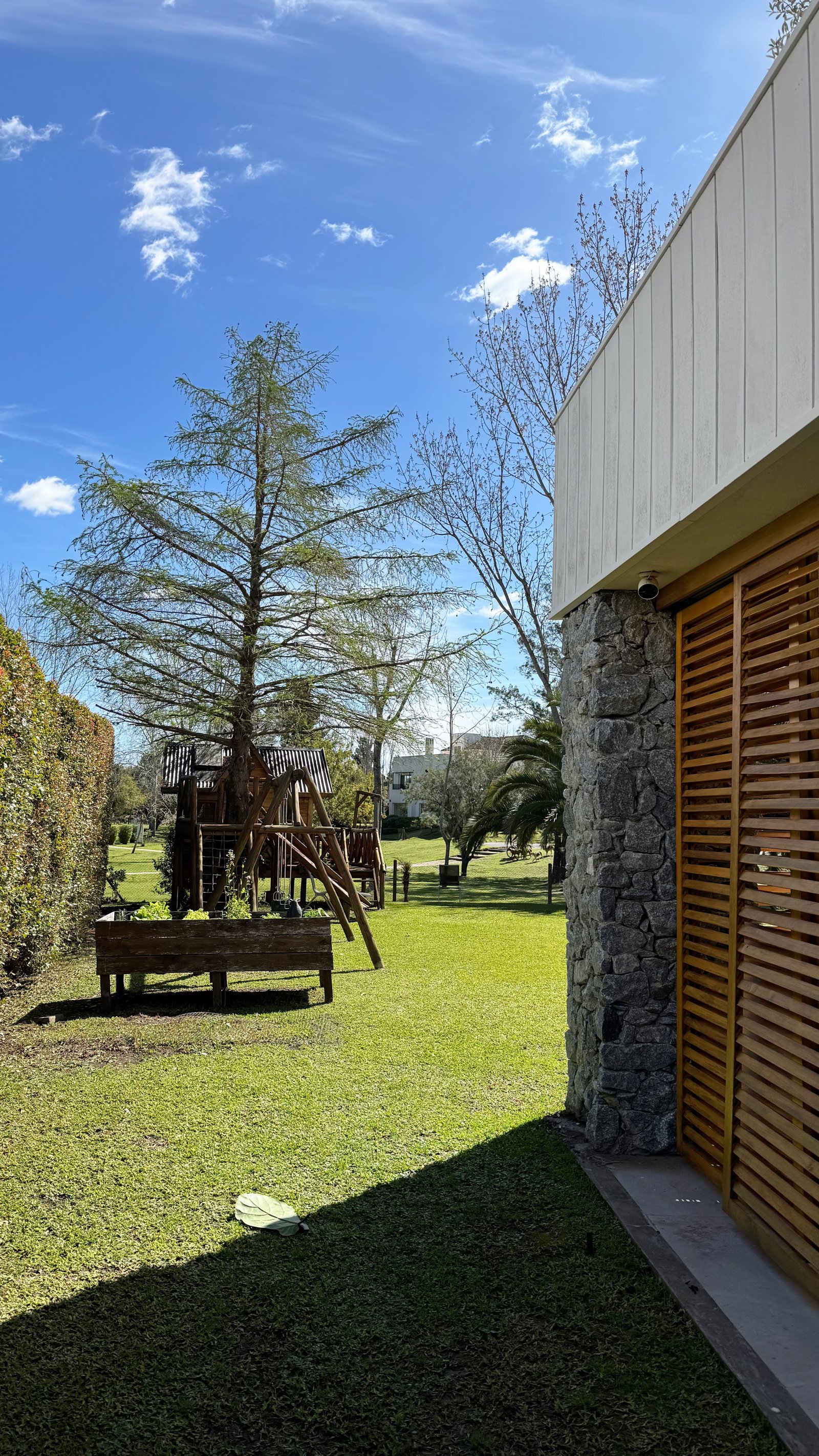 Jardín moderno con casa de piedra y madera, y juegos infantiles — proyecto CASA CM, por Hermann Arquitectos, en Los Castores
